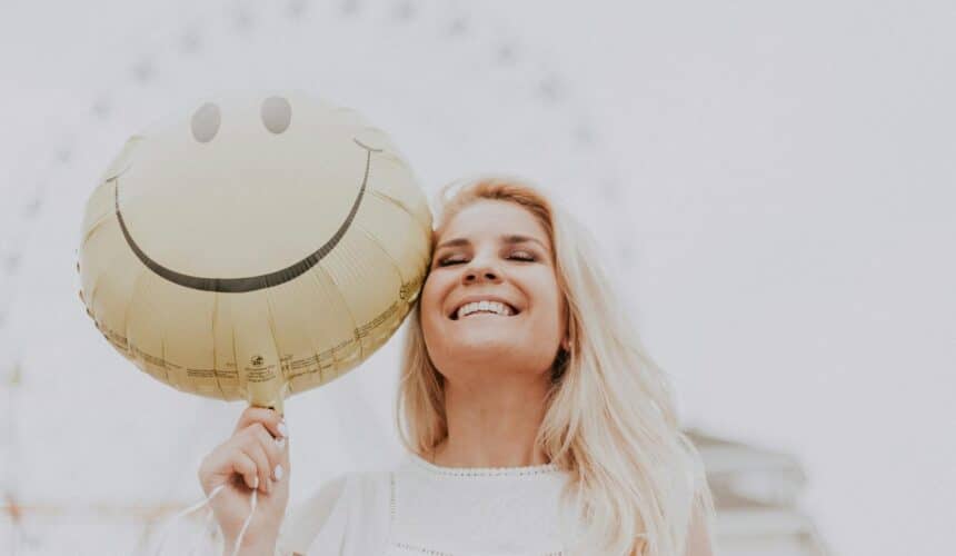 Fröhliche Frau, die an einem sonnigen Tag im Freien einen Smiley-Ballon hält und Glück und Positivität ausstrahlt.