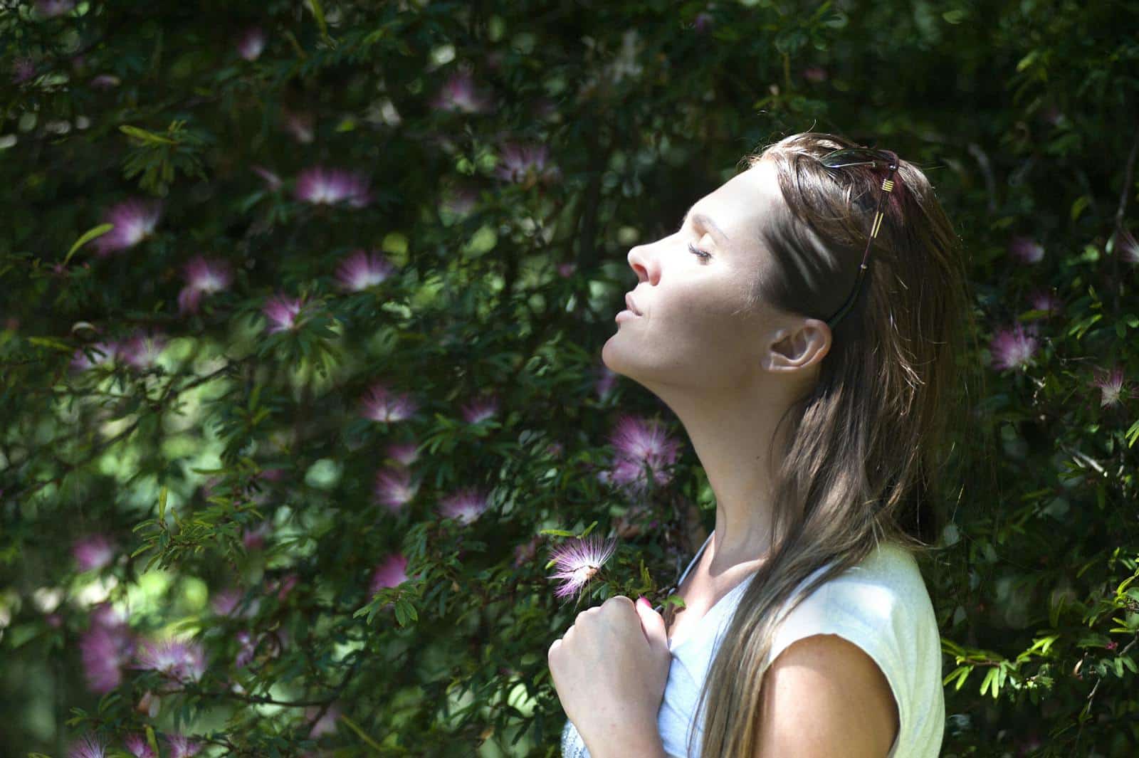 Una mujer disfruta de un momento de serenidad en un jardín iluminado por el sol, rodeada de flores vibrantes.