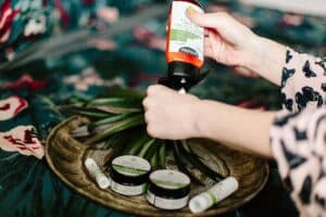 Nahaufnahme einer Frau, die CBD-Lotion aufträgt, umgeben von Wellnessprodukten auf einem dekorativen Teller.