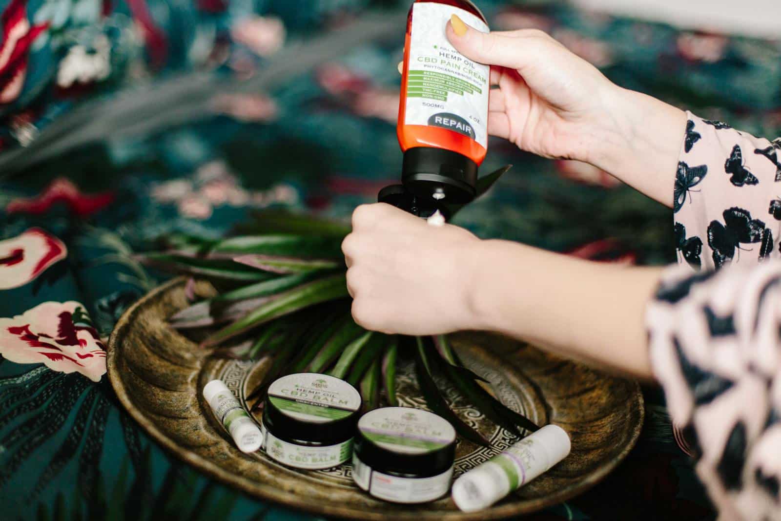 Close-up shot of a woman applying CBD lotion, surrounded by wellness products on a decorative plate.