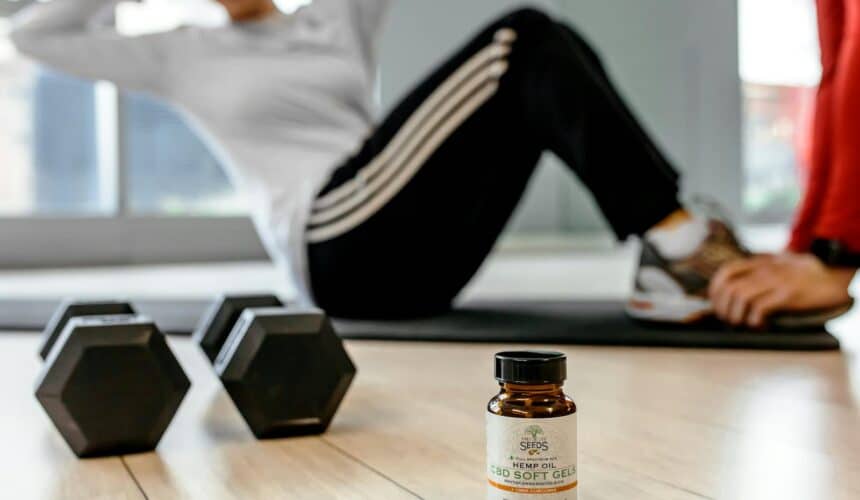 Focused image of CBD soft gels bottle on gym floor with person exercising in the background.