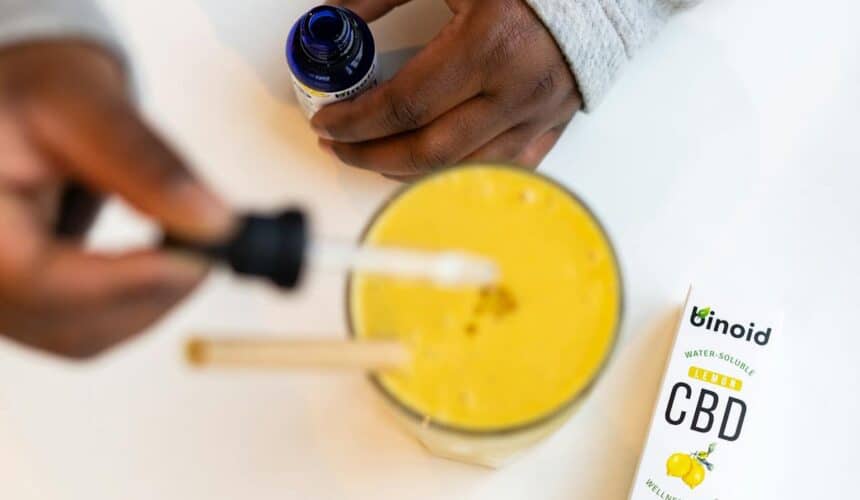 Close-up of hands using CBD oil with lemon smoothie, emphasizing wellness.