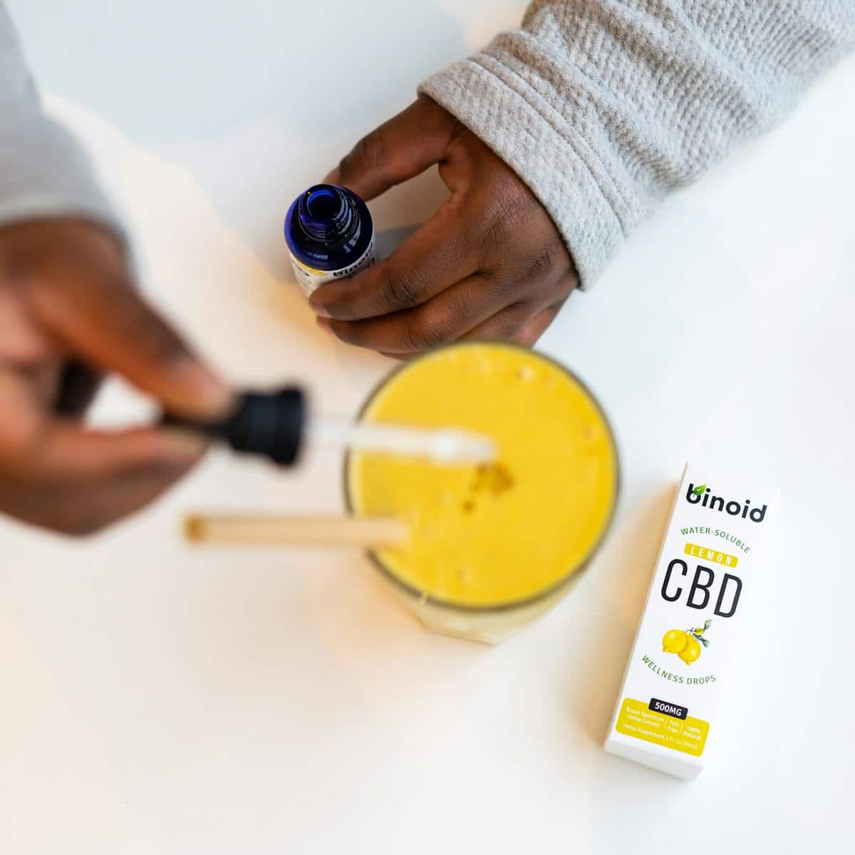 Gros plan des mains utilisant de l'huile de CBD avec un smoothie au citron, mettant l'accent sur le bien-être.