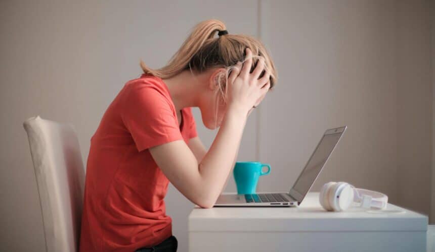 Junge Frau fühlt sich gestresst, während sie zu Hause mit Laptop und Kaffeetasse lernt.