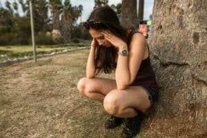 Eine Frau kniet in einem Park neben einem Baum und hält ihren Kopf, um ihren Stress oder ihre Angst auszudrücken.
