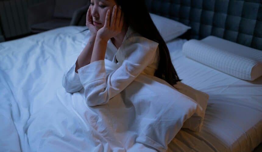 Eine asiatische Frau liegt nachts im Bett, leidet unter Schlaflosigkeit und Einsamkeit und ist in Gedanken versunken.