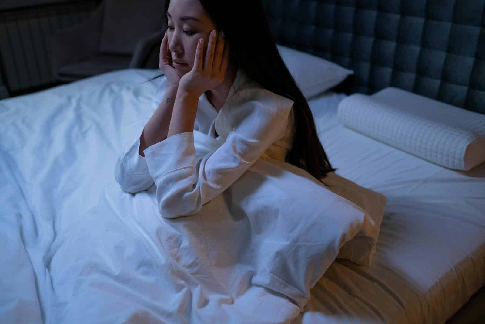 Una donna asiatica a letto di notte, che soffre di insonnia e solitudine, immersa nei suoi pensieri.