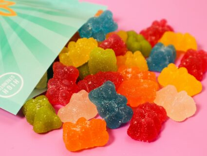 CBD gummy bears spilling out of a high-strength package on a pink surface.